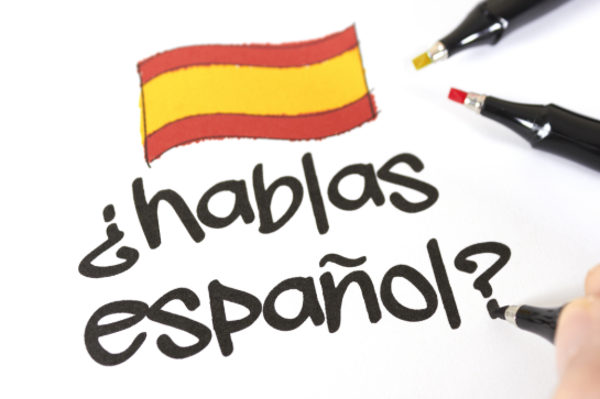 Hand schrijft de vraag "¿hablas español?" met een Spaanse vlag erboven op wit papier. (vergroot foto)
