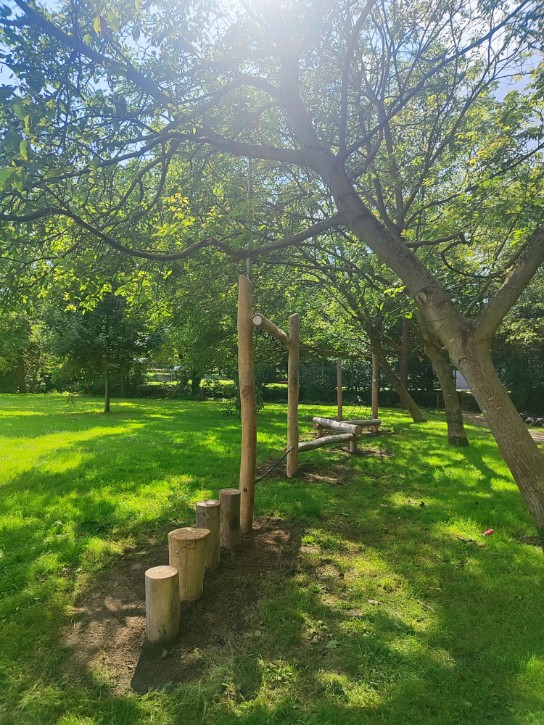 Speeltoestel van hout in een zonnig, groen park met bomen en gras.