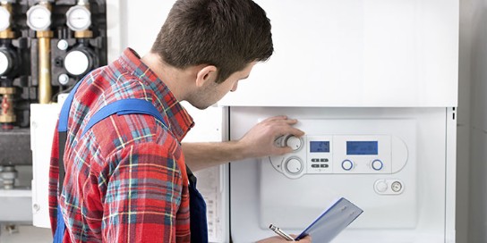 Man in geruit overhemd stelt thermostaat van cv-ketel in met notitieboekje in de hand. (vergroot foto)